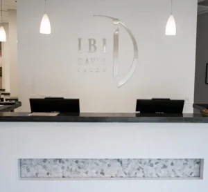 - Ibi David Salon in Westlake, OH Reception desk with two computer monitors and a sign on the wall reading "IBI David Salon," under three hanging pendant lights. - Ibi David Salon in Westlake, OH