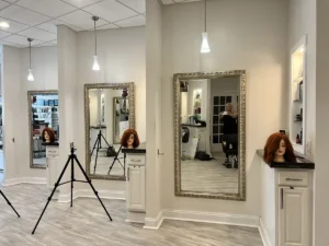- Ibi David Salon in Westlake, OH A modern hair salon with three mirrors, mannequin heads with red hair on stands and counters, and a person’s reflection taking a photo. - Ibi David Salon in Westlake, OH