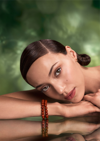 - Ibi David Salon in Westlake, OH A woman with smooth, dark hair rests her head on her arm, wearing a red beaded bracelet, against a blurred green background. Her reflection is visible on the surface below. - Ibi David Salon in Westlake, OH